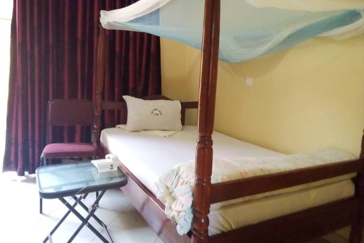 Een enkel bed met houten frame en een hemelbed, een tafeltje met een stoel, en een kussen op het bed.
