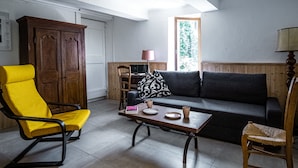 Una sala de estar con un sillón amarillo, un sofá oscuro, una mesa de madera y un aparador de madera.
