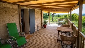 Un espacio al aire libre techado con una terraza de madera, una mesa con sillas y vistas a zonas verdes.