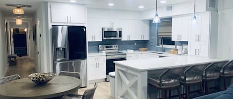 A modern kitchen with white cabinets, stainless steel appliances, and a central island with bar stools.