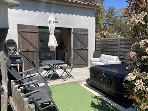 Un espace patio aménagé avec une table et des chaises, un parasol blanc, un jacuzzi et une clôture en bois.