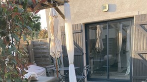 Un espace patio agrémenté d’une clôture en bois, d’un jacuzzi et d’un coin salon avec des chaises et des parasols.