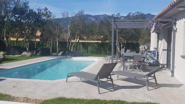 Une piscine dotée de chaises longues et d’une pergola, entourée d’un jardin et offrant une vue sur la montagne.