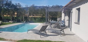 Une piscine dotée de chaises longues et d’une pergola, entourée d’un jardin et offrant une vue sur la montagne.