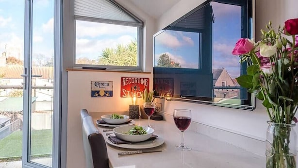 A dining area with a table set for two, a vase of flowers, and a view of the outside. - Papillon, a modern Southwold flat with balcony (Southwold)