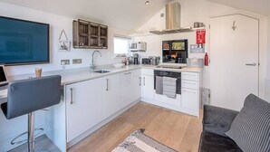 A modern kitchen with white cabinets, a bar stool, a microwave, and a coffee machine. - Papillon, a modern Southwold flat with balcony (Southwold)