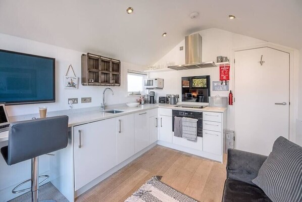 A modern kitchen with white cabinets, a bar stool, a microwave, and a coffee machine. - Papillon, a modern Southwold flat with balcony (Southwold)