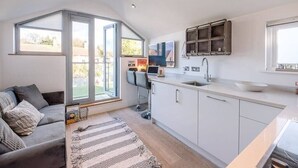 A modern kitchen with white cabinets, a built-in sink, and a window overlooking a garden. - Papillon, a modern Southwold flat with balcony (Southwold)