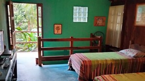 Una habitación con dos camas, un escritorio de madera, un ventanal con vistas a zonas verdes y un techo con vigas a la vista.