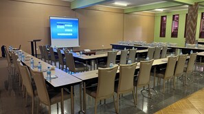 A conference room with a large screen displaying a presentation, arranged tables with chairs, and water bottles on each table.