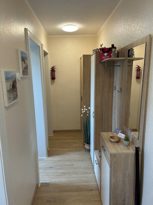 A hallway with wooden flooring, a wooden cabinet with a mirror, and a fire extinguisher on the wall. - Ritthoff Perlebucht Vacation Rental - Beach chairs by the sea & free admission to the pool* (Büsum)