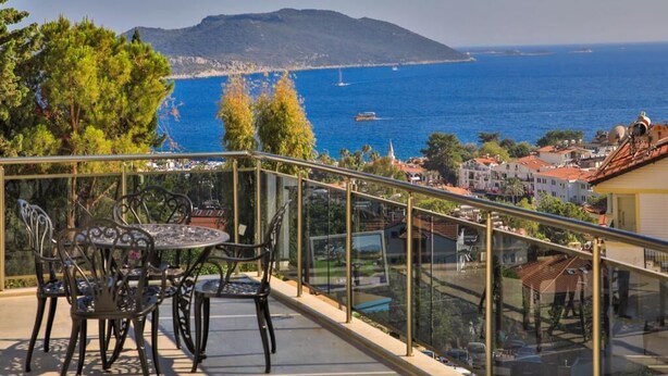 En balkon med gelænder i glas, der ud til et kystlandskab med et bjerg i baggrunden.