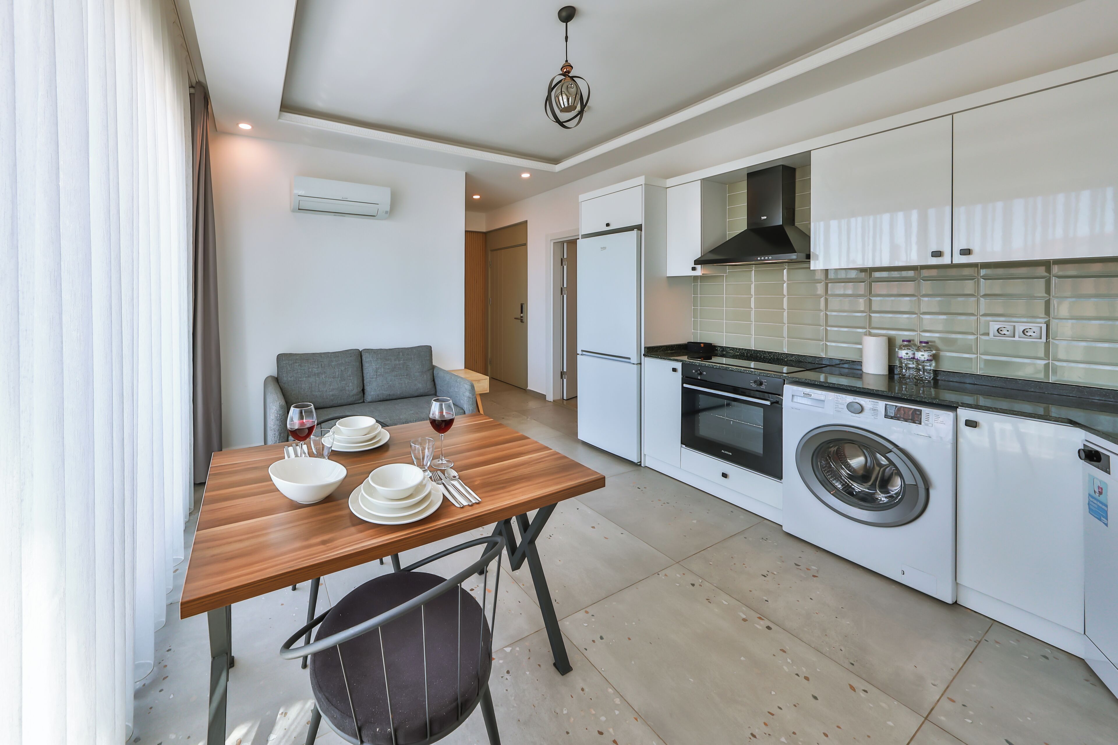 A compact kitchen with a washing machine, a dining table with chairs, and a sofa.
