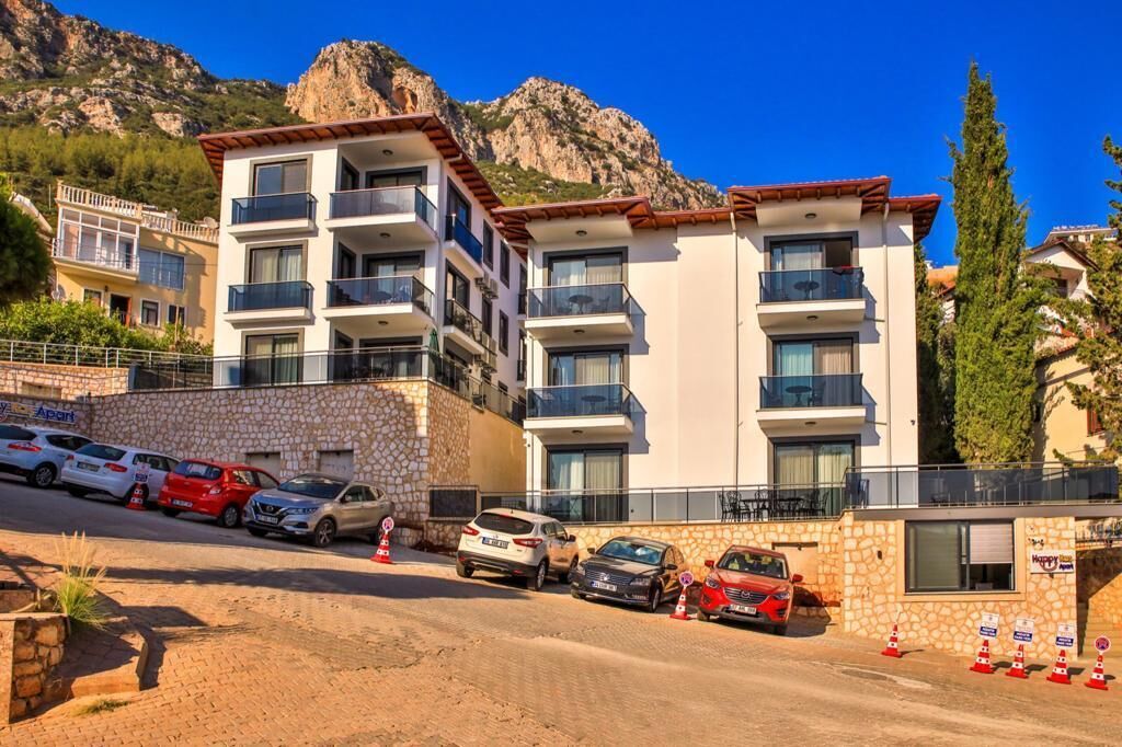 A multi-story hotel with balconies, a stone facade, and a mountainous backdrop.