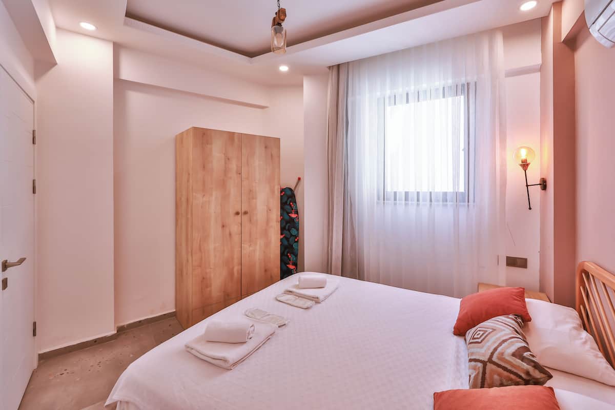 Une chambre d’hôtel avec un grand lit, une armoire, une fenêtre avec des rideaux légers et un luminaire fixé au mur.