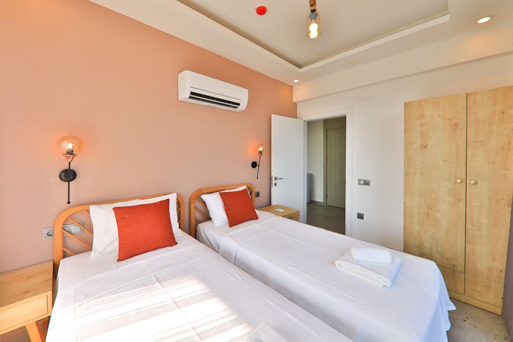 A hotel room with two beds, a wardrobe, an air conditioning unit, and a nightstand with a lamp.