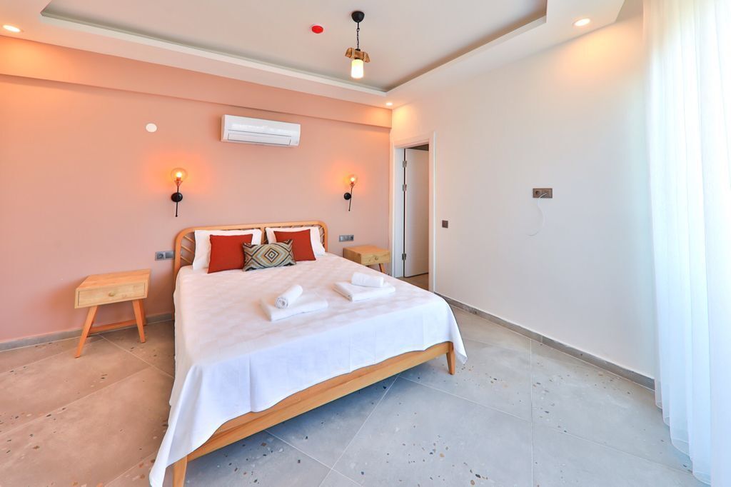 A bedroom with a bed, bedside tables, wall-mounted lights, and an air conditioning unit.
