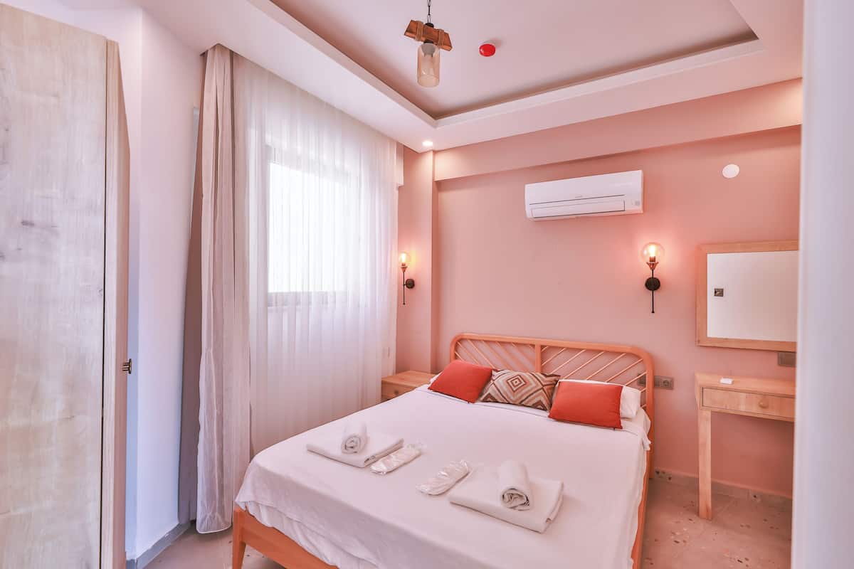 Un lit bien fait, avec des serviettes, une table de chevet, une commode, un miroir et un appareil de climatisation fixé au mur.