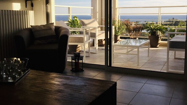 Un salon moderne doté d’une grande porte-fenêtre coulissante donnant sur un balcon avec vue sur la mer.