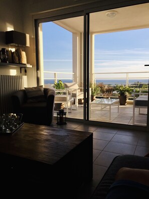 Un salon moderne doté d’une grande porte-fenêtre coulissante donnant sur un balcon avec vue sur la mer.