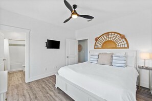 A bedroom with a bed, a ceiling fan, a mounted TV, and a decorative wall piece.