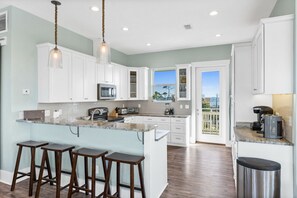 A modern kitchen with white cabinets, a large island with stools, a microwave, and a coffee machine.