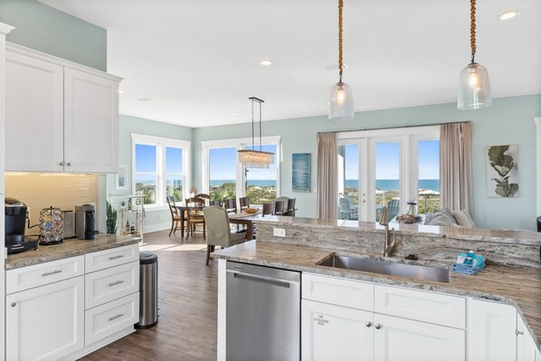 A modern kitchen with a central island, stainless steel appliances, and a view of the ocean through large windows.