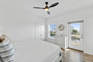 A bedroom with a bed, a ceiling fan, a dresser, a window, and a door leading to a balcony.