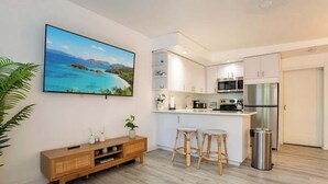 Een moderne keuken met witte kastjes, een roestvrijstalen koelkast en een zithoek met een barstoel.
