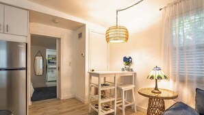 Een moderne keuken met een koelkast, een witte tafel met planken, een hanglamp en een kleine ronde tafel met een lamp.