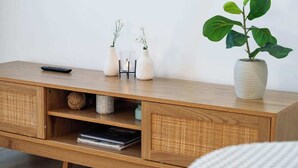 Een houten console tafel met een afstandsbediening, twee witte vazen met witte bloemen en een potplant.