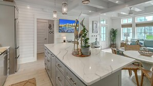 Una cocina moderna con una isla de mármol, luces colgantes y un televisor grande.