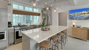 Una cocina moderna con una isla grande, electrodomésticos de acero inoxidable y un amplio ventanal con vista a una piscina.