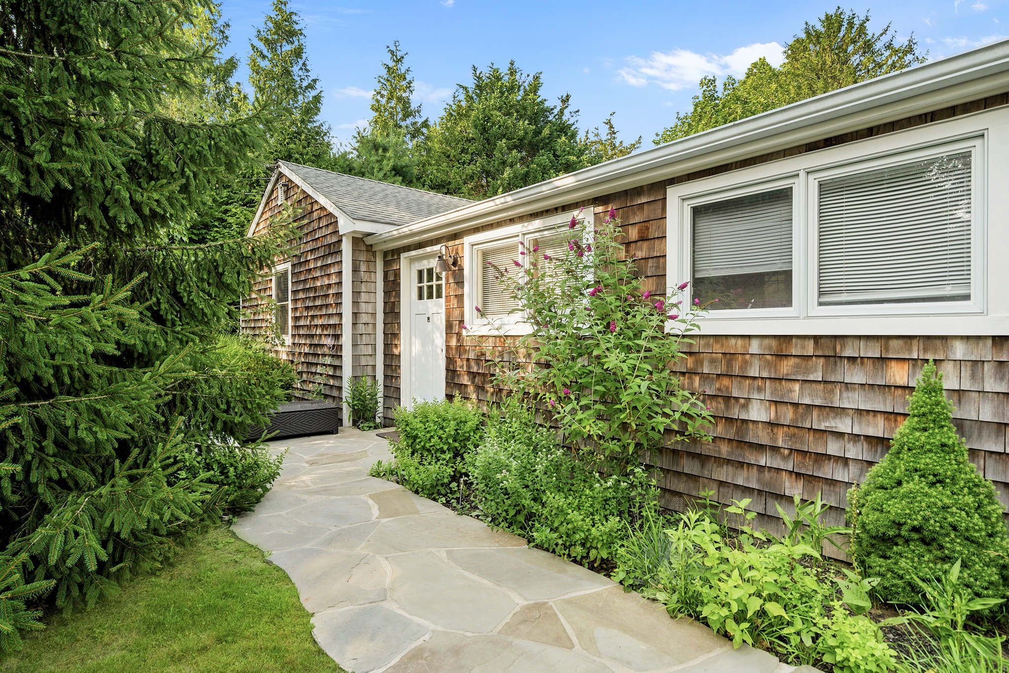 A residential property with a stone pathway leading to a wooden house with a shingled exterior.