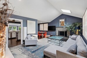 Una sala de estar moderna con sofá, mesa de centro y chimenea. Hay un comedor con sillas y un televisor montado en la pared.