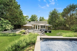 Un jardin avec une piscine, des meubles de patio et un espace salon abrité.