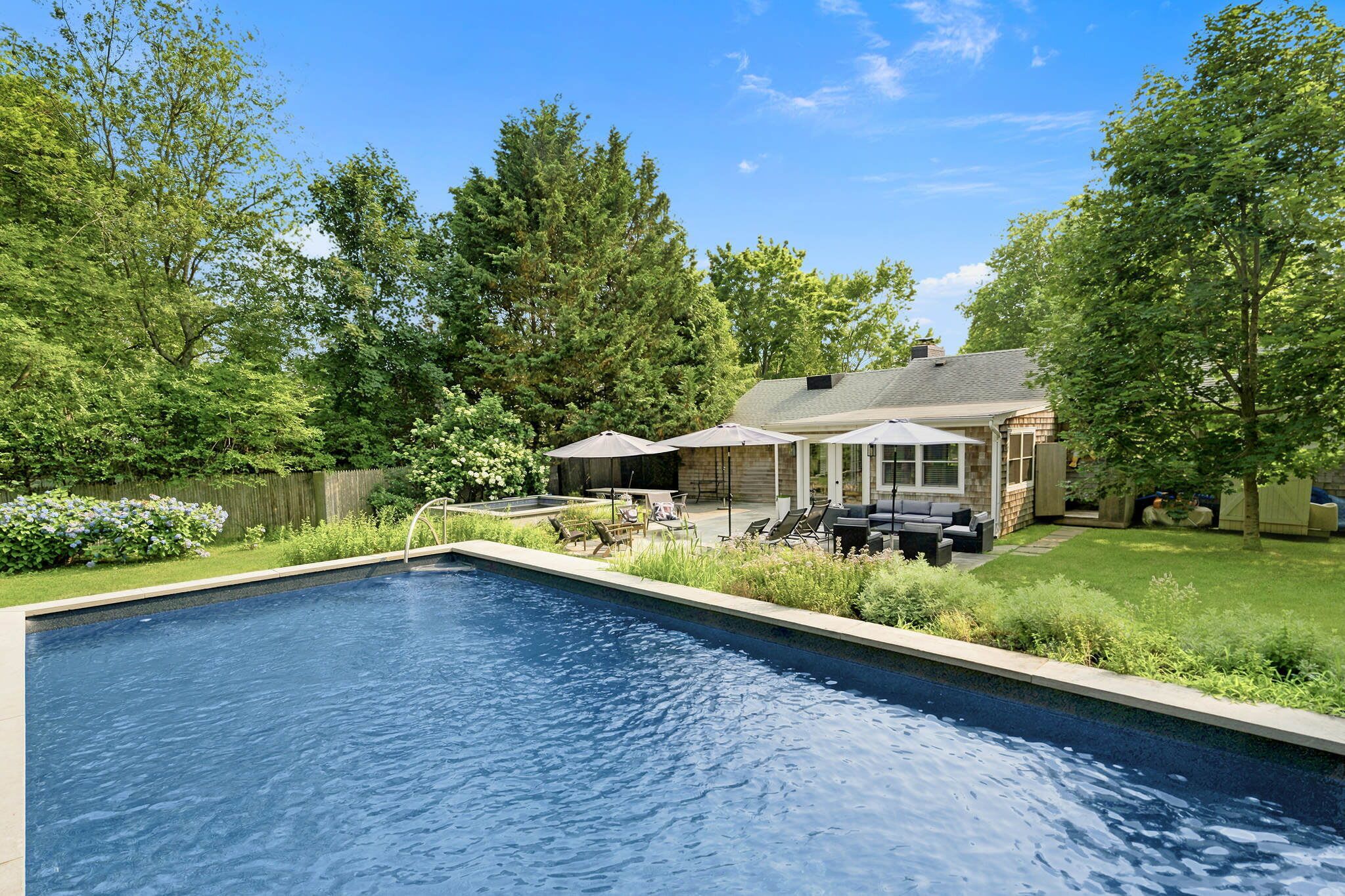 A swimming pool with a patio area, a covered seating area, and a house in the background.