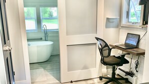 A modern bathroom with a bathtub, a shower, and a toilet. There is a desk with a laptop and a chair. - Lakeview retreat with beach access. Stylish home just steps from Deep Run Beach. (Canandaigua)