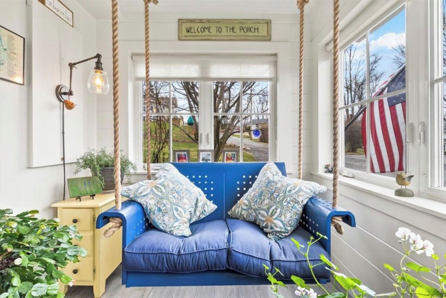 Un porche acogedor con un sofá azul, una lámpara colgante y un letrero que dice 'Welcome to the Porch'.