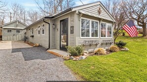 A single-story house with a garage, a front porch, and a small front yard with a flag. - Lakeview retreat with beach access. Stylish home just steps from Deep Run Beach. (Canandaigua)