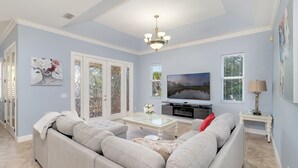 A spacious living room with a sectional sofa, a glass coffee table, a flat-screen TV, and a chandelier. - "Pelican Nest"Private Beach & Bay access & Pool 4bedroom 3bath (Englewood)