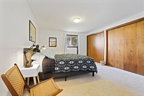 Quarto com cama, mesa de cabeceira, abajur, cadeira, guarda-roupa e janela.