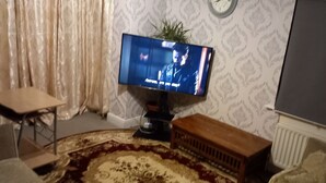 Olohuone, jossa on televisio, pieni pöytä, penkki ja kuviollinen matto.