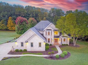 A two-story house with a stone facade, a large front porch, and a well-maintained lawn.