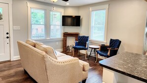 Un salon moderne avec un canapé beige, des fauteuils bleus, une table basse en bois et un ventilateur de plafond.