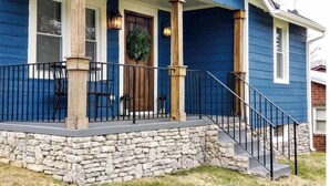 Une maison bleue avec des fondations en pierre, un porche doté d’une balustrade et une porte ornée d’une guirlande.