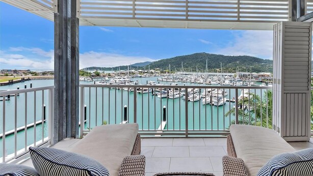 A balcony with a view of a marina and hills in the distance.