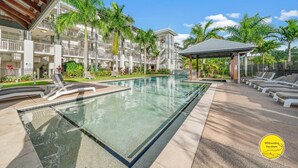 A hotel pool area with a clear pool, sun loungers, and a covered seating area.
