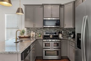 Cozinha moderna com eletrodomésticos de aço inoxidável, armários cinza, painel de azulejos e bancada de granito.