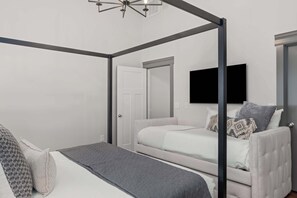 Quarto com cama de dossel, televisão na parede e porta que dá para outro cômodo.